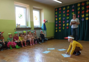 Dzieci odgadują wiosenne zagadki poprzez podniesienie właściwego obrazka z podłogi do góry.