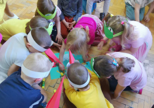 Dzieci wyklejają szablony przebiśniegów białymi guzikami, watą i zielonymi pomponami.