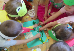 Dzieci wyklejają szablony przebiśniegów białymi guzikami, watą i zielonymi pomponami.