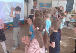 Dzieci stoją i klaszczą w rytm muzyki.