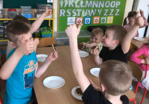 Dzieci siedzą przy stole podczas jedzenia kanapki z własnoręcznie wykonaną zdrową nutellą, unoszą kciuk w górę.