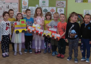 Dzieci trzymają w rękach pociąg zrobiony z kolorowych kartonów, a w nim obrazki zdrowych produktów.