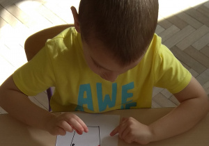 Chłopiec wykleja szablon kubka małymi kuleczkami plasteliny.