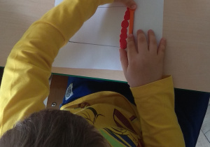 Dziecko wykleja szablon kubka kolorowymi kuleczkami plasteliny.