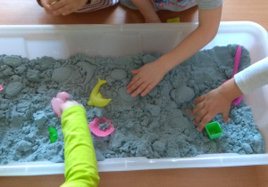 Dzieci odkopują skarby ukryte w piasku kinetycznym.
