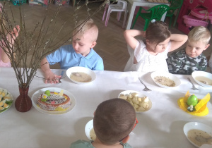 Dzieci siedzą przy stole i zjadają świąteczne śniadanie: barszcz biały z kiełbaską i jajkiem.