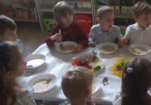 Dzieci siedzą przy stole i zjadają świąteczne śniadanie: barszcz biały z kiełbaską i jajkiem.