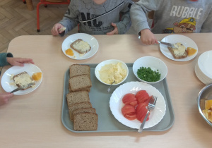 Dzieci smarują pieczywo i nakładają sobie wybrane produkty: wędlina, warzywa, owoc.