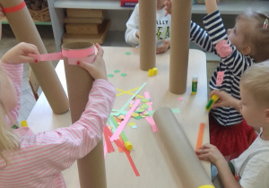 Dzieci ozdabiają eko instrument, naklejając na niego kolorowe paski i kółeczka.