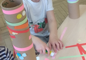 Dzieci ozdabiają eko instrument, naklejając na niego kolorowe paski i kółeczka.