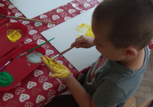 Chłopiec maluje dłoń żółtą farbą.