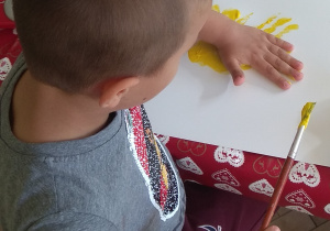 Chłopiec odbija farbę z dłoni na kartonie.