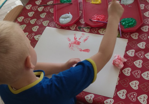 Chłopiec wybiera kolor farby do namalowania palcem łodygi i liści.