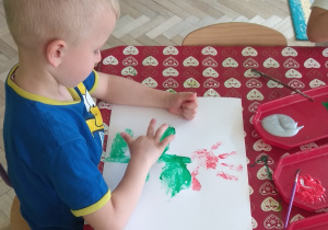 Chłopiec maluje palcem na kartonie liście kwiatu.