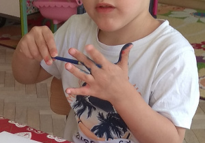 Chłopiec nakłada pędzlem niebieską farbę na dłoń.