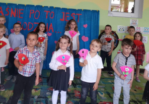 Dzieci stoją na scenie trzymając w rękach papierowe wachlarze ozdobione kwiatami.