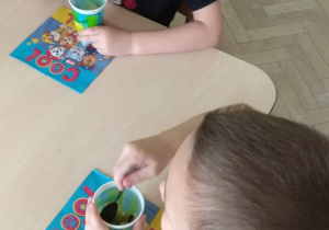 Dzieci jedzą samodzielnie zrobioną sałatkę z owoców.