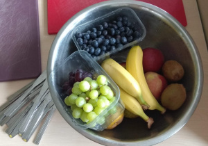 Na stole stoi miska z owocami, obok leżą noże.
