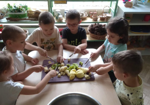 Dzieci w 6 osobowych grupkach kroją owoce na sałatkę owocową.