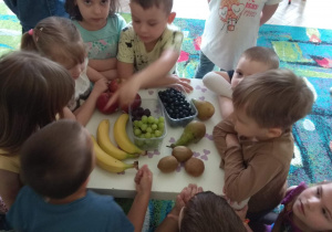 Dzieci nazywają i przeliczają kolejno owoce ułożone na stoliczku.