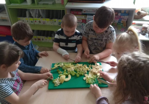 Dzieci w 6 osobowych grupkach kroją owoce na sałatkę owocową.
