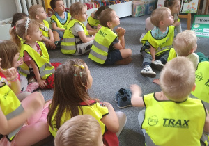 Dzieci siedzą w bibliotece i uważnie słuchają.