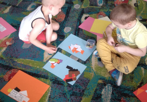 Na dywanie na kartonach leżą figury geometryczne, chłopcy wybierają po jednej figurze z każdego rodzaju: trójkąt, koło, kwadrat i prostokąt.