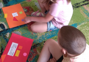 Dzieci na swoich kartonach układają figury geometryczne i pojazd.