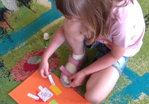 Dziewczynka układa napisy: na, pod, obok, nad przy figurach na swioim kartonie.