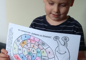 Chłopiec pokazuje pokolorowaną grę - dodawanie ze ślimakiem.