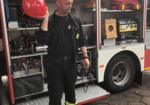 Strażak demonstruje wyposażenie wozu strażackiego.