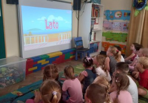 Dzieci oglądają na tablicy multimedialnej prezentację o lecie.