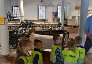 Dzieci stoją przy maszynach tkackich.