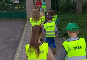 Dzieci wracają z pieszej wycieczki. Zatrzymują się przed znakiem informującym o nazwie przedszkola.
