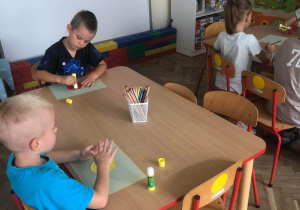 Dzieci siedzą przy stoliku wykonując pracę plastyczną