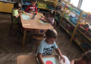 Dzieci siedzą przy stoliku wykonując pracę plastyczną