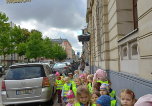 Dzieci stoją na chodniku przed Teatrem w parach, oczekując na autobus.