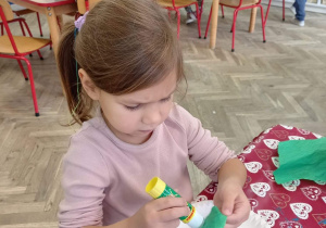 Dziewczynka przykleja bibułę na papierowy talerzyk.