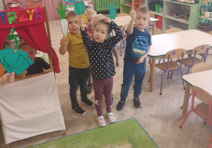Dzieci stoją i pokazują kukiełkowe warzywa.