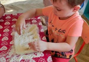 Dziecko miesza mąkę z wodą.