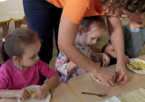 Dzieci z pomocą nauczycielki zawijają ciasto.