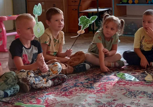 Dzieci siedzą na dywanie, trzymając kukiełki.