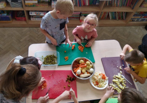 Dzieci i rodzice kroją warzywa.