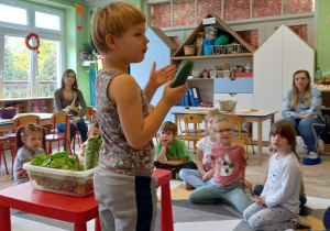 Chłopiec pokazuje dzieciom ogórka, wszyscy dzielą nazwę warzywa na sylaby.