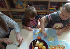 Dzieci i starsza siostra jednego z przedszkolaków kroją warzywa.