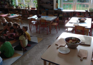 Dzieci siedzą na dywanie, na stołach czekają ugotowane warzywa, miski oraz deski do krojenia.