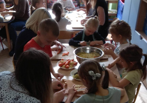 Dzieci wraz z rodzicami kroją warzywa na sałatkę.