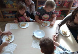Dzieci wraz z rodzicami jedzą sałatkę.