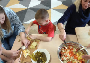 Dzieci wraz z rodzicami kroją warzywa na sałatkę.