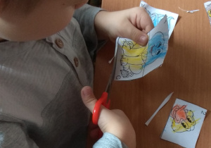 Dziecko wycina nożyczkami obrazki po linii prostej.